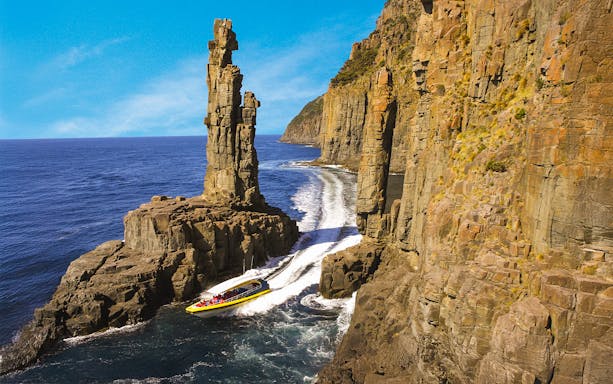 Boat navigating between towering sea cliffs on Bruny Island Wilderness Cruise.