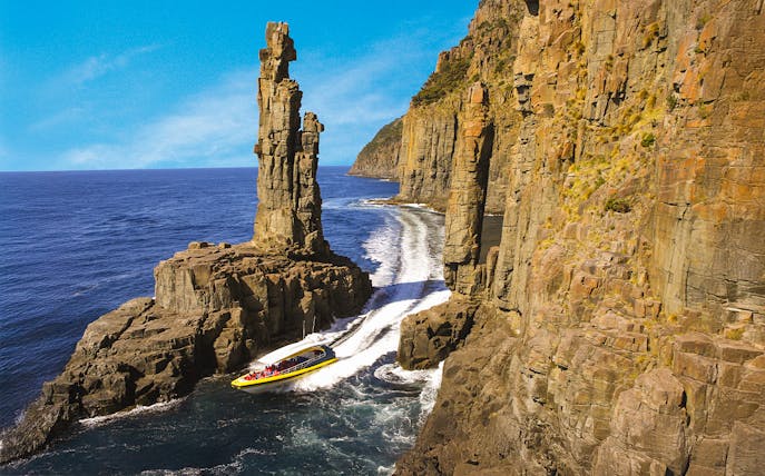 Boat navigating between towering sea cliffs on Bruny Island Wilderness Cruise.