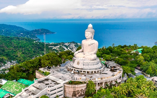 Big Buddha statue overlooking lush hills and ocean in Phuket, Thailand.