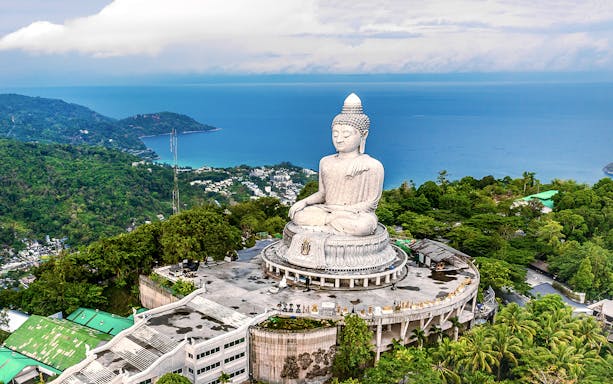 Big Buddha statue overlooking lush hills and ocean in Phuket, Thailand.