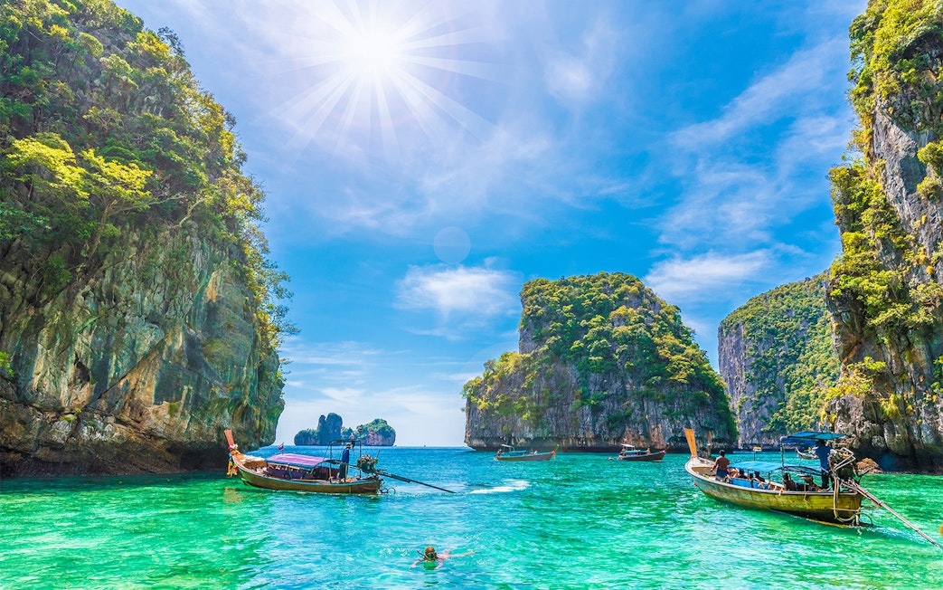 Longtail boats in Loh Samah Bay, Phi Phi, with limestone cliffs and clear water.