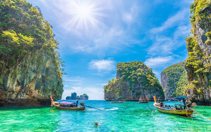 Longtail boats in Loh Samah Bay, Phi Phi, with limestone cliffs and clear water.