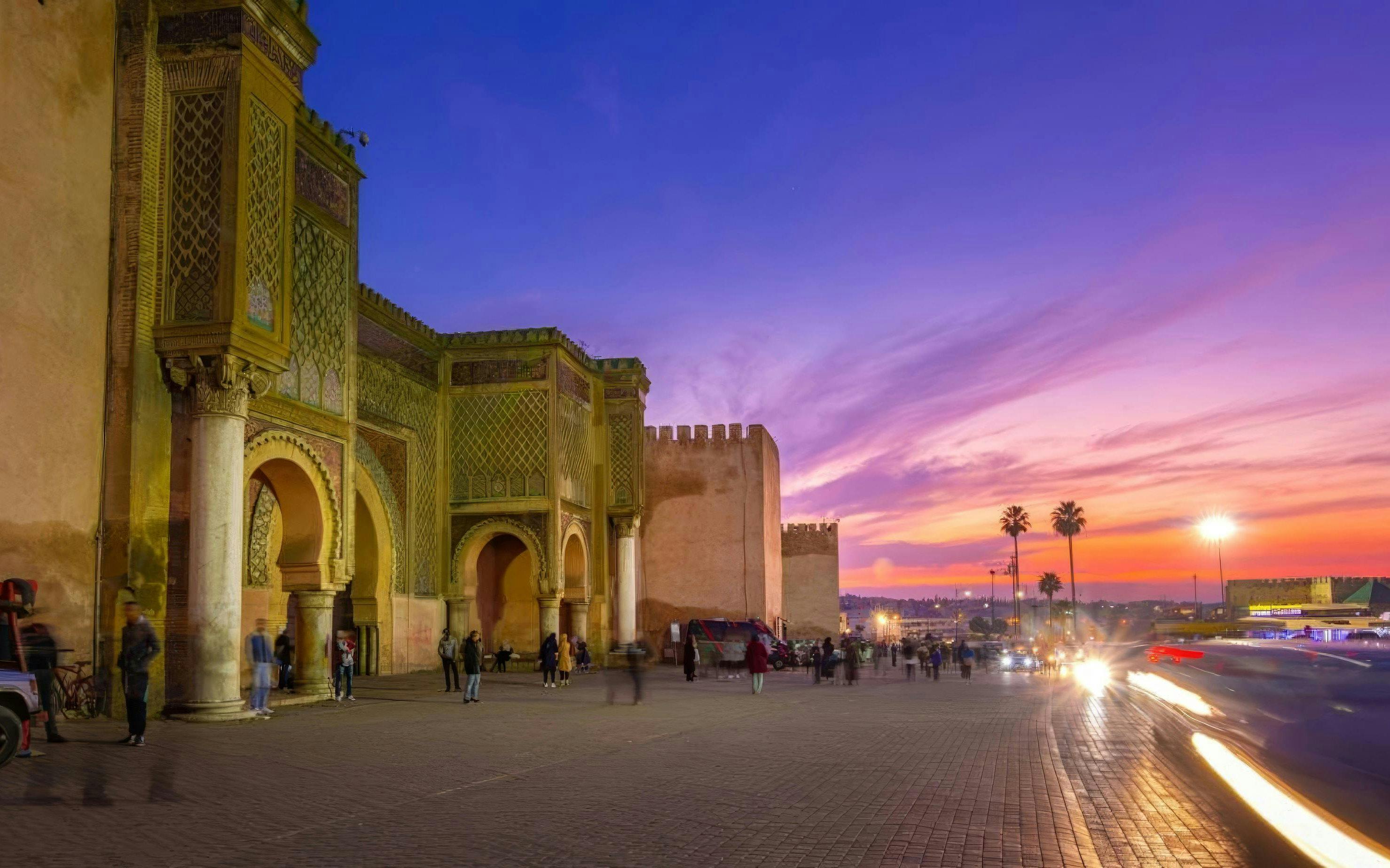 Bab Mansour Gate in Meknes at sunset with people walking nearby.