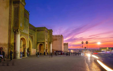 Bab Mansour Gate in Meknes at sunset with people walking nearby.