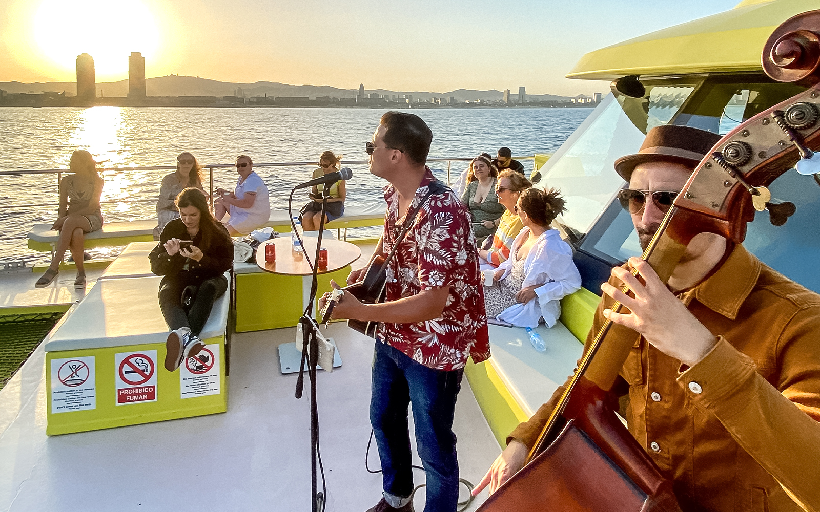 Tourists enjoying live music on a catamaran cruise at sunset in Barcelona.