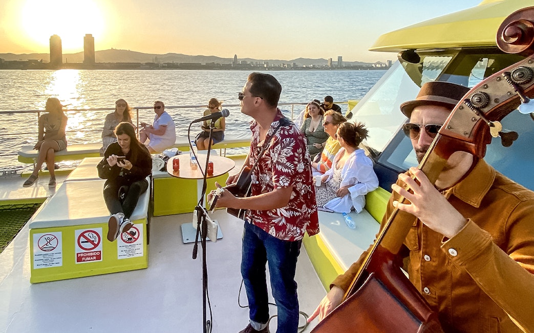 Tourists enjoying live music on a catamaran cruise at sunset in Barcelona.