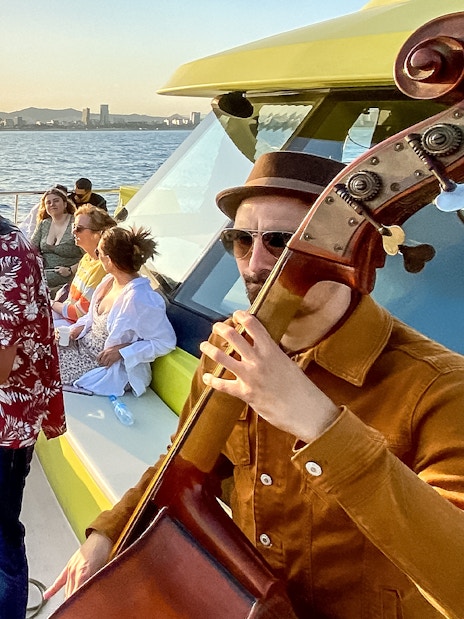 Tourists enjoying live music on a catamaran cruise at sunset in Barcelona.