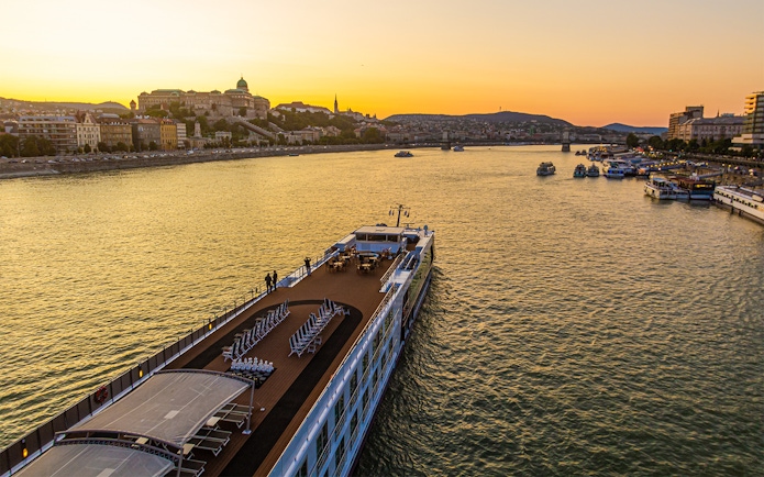 Cruise ship on the Danube River at sunset with Budapest skyline in the background.