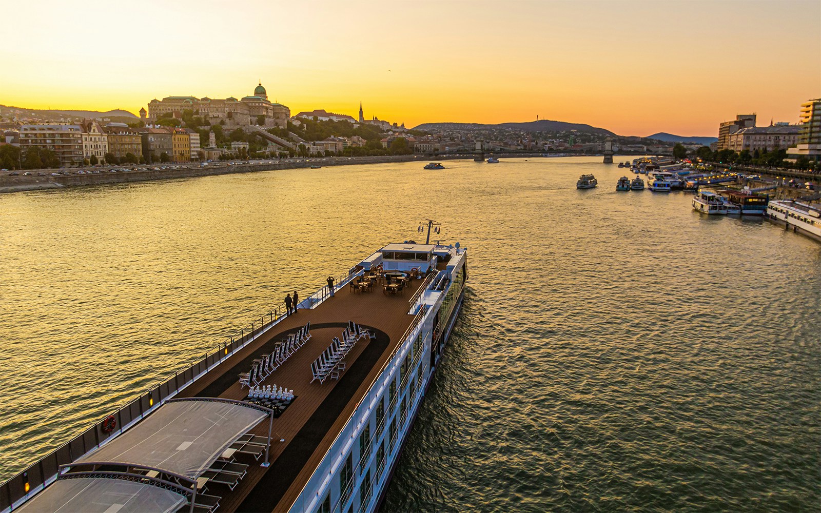 Cruise ship on the Danube River at sunset with Budapest skyline in the background.
