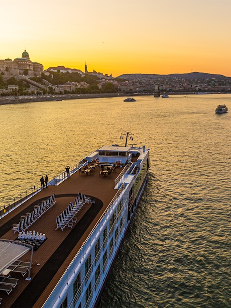 Cruise ship on the Danube River at sunset with Budapest skyline in the background.