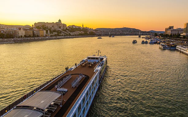 Cruise ship on the Danube River at sunset with Budapest skyline in the background.