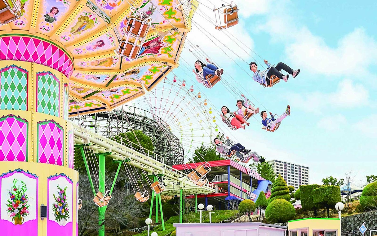 Visitors enjoying a swing ride at Hirakata Park, Japan, with a roller coaster in the background.