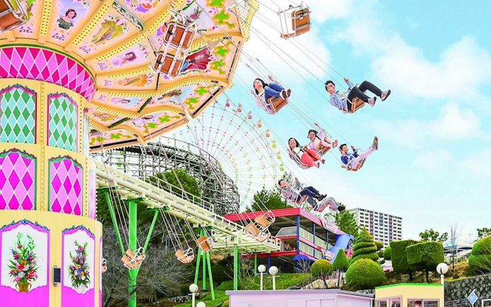 Visitors enjoying a swing ride at Hirakata Park, Japan, with a roller coaster in the background.