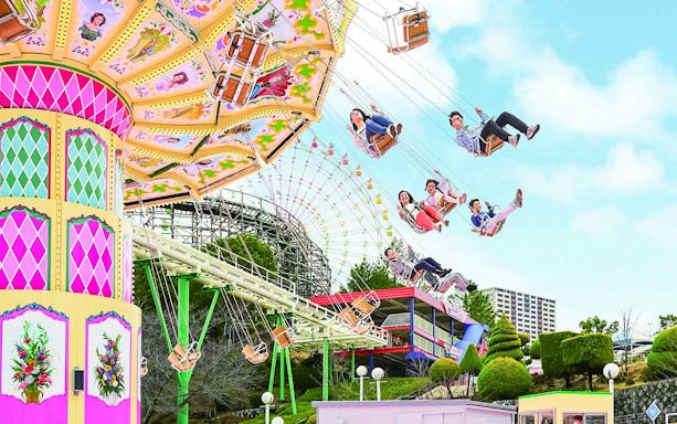 Visitors enjoying a swing ride at Hirakata Park, Japan, with a roller coaster in the background.