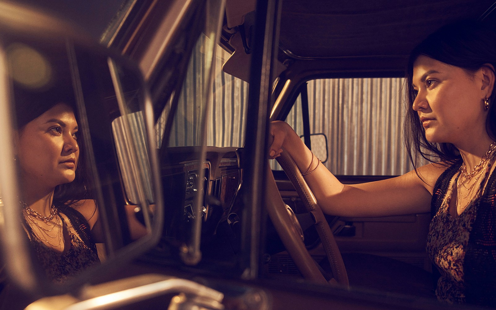 Person sitting in a car, looking at their reflection in the rearview mirror.