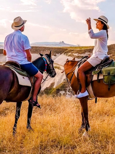 Guests horseback riding at sunset in Cappadocia with scenic rock formations.