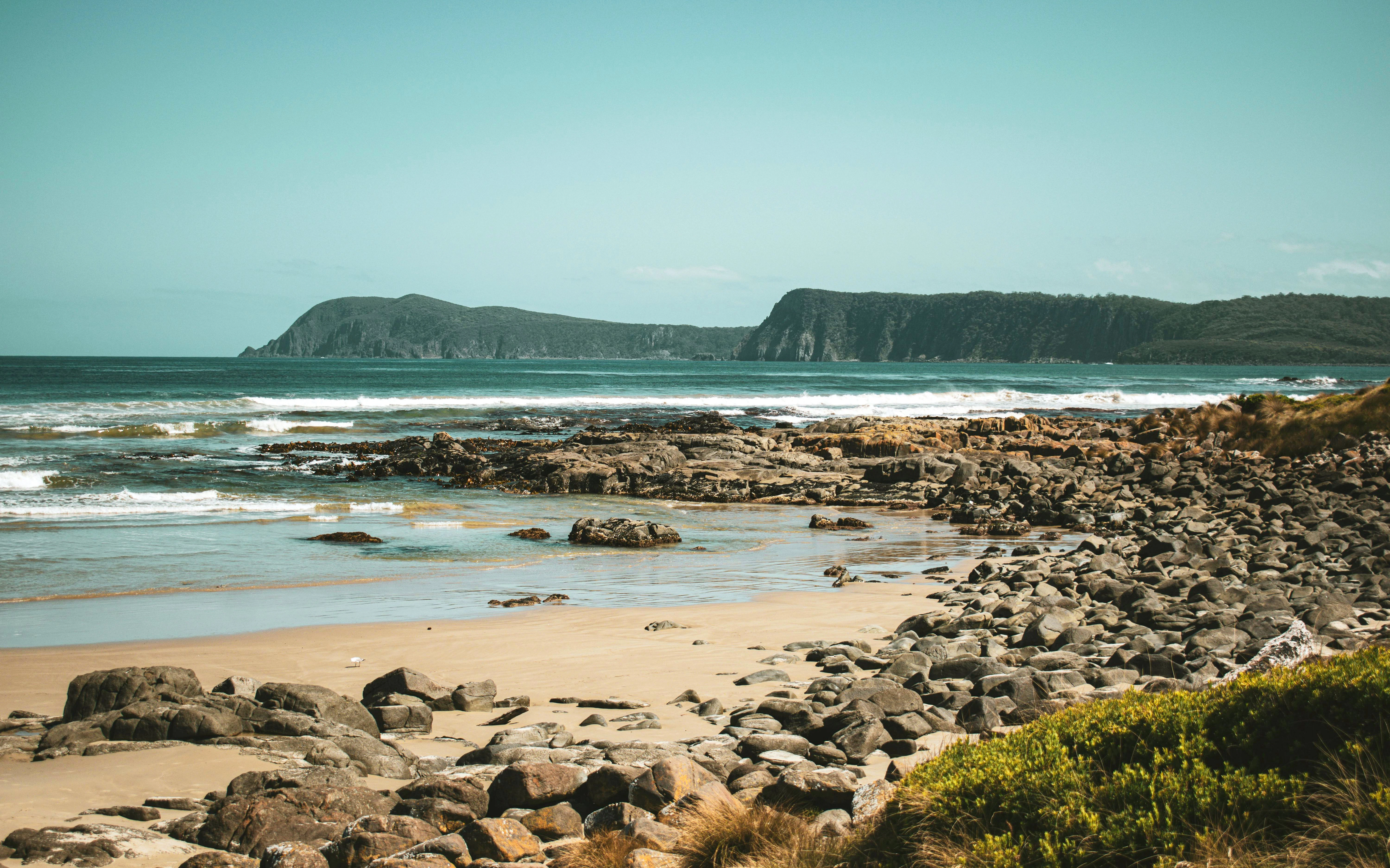 Rocky shoreline with ocean waves and distant cliffs on Bruny Island, Australia.