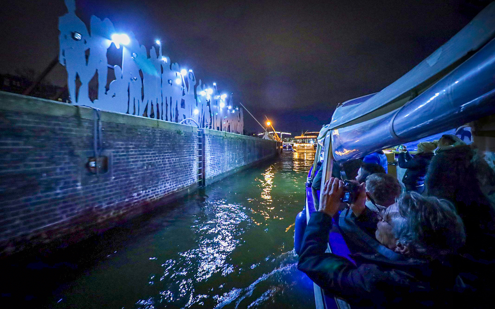 Guests on a boat photographing illuminated installations at Amsterdam Light Festival.