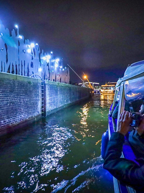 Guests on a boat photographing illuminated installations at Amsterdam Light Festival.