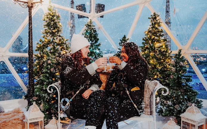 Guests toasting inside the Up at the O2 Snow Globe Experience with festive trees.