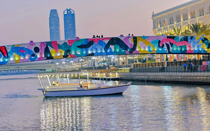 Boat cruising under colorful bridge in Sharjah during evening tour.