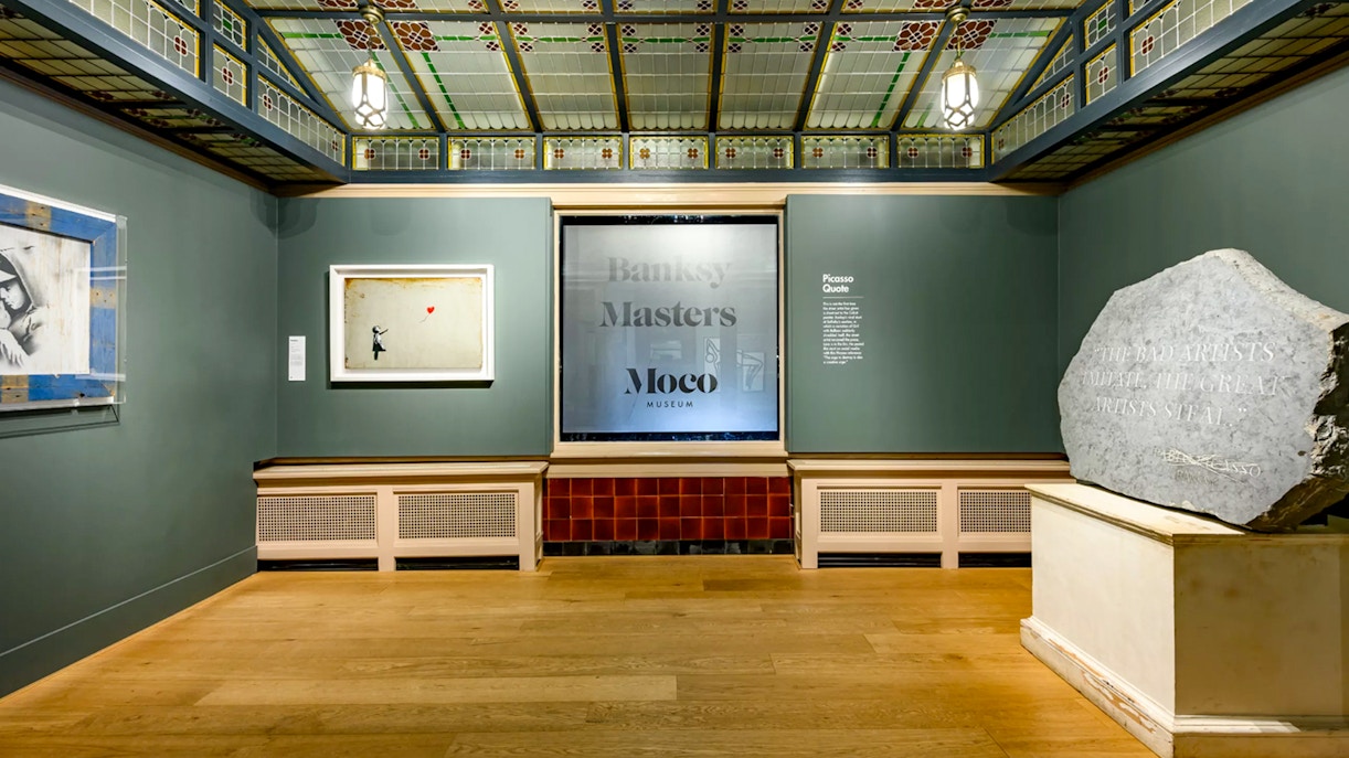 Moco Museum Amsterdam Banksy exhibit with framed artwork and Picasso quote on stone.