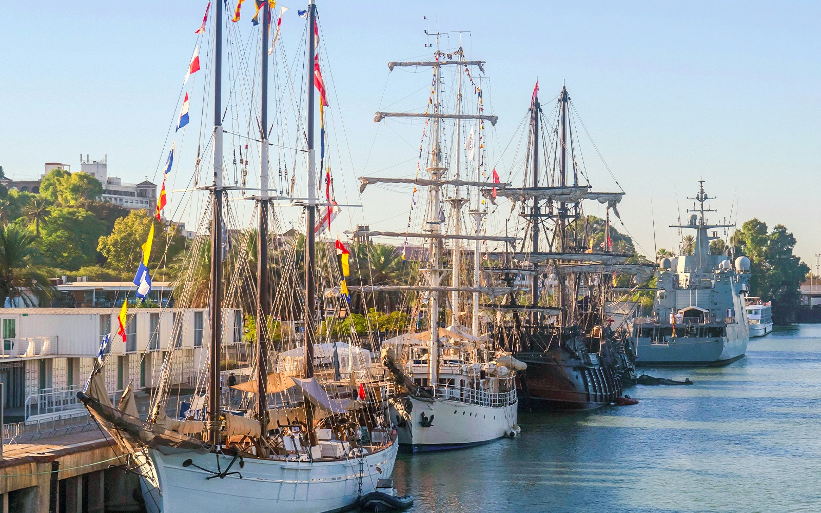 Boats moored at the pier in a scenic harbor, with a backdrop of lush green hills.