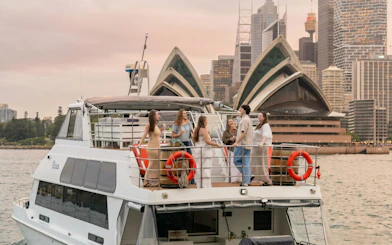Group enjoying drinks on a boat with Sydney Opera House in the background.