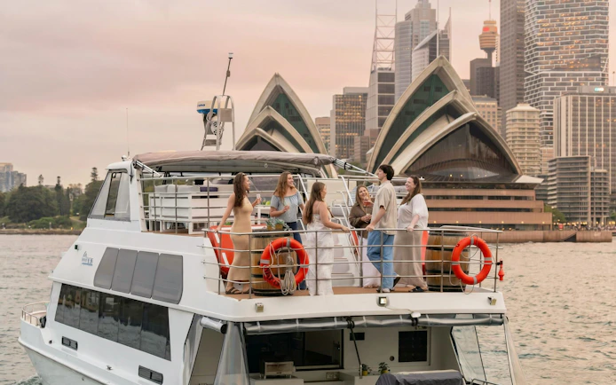 Group enjoying drinks on a boat with Sydney Opera House in the background.