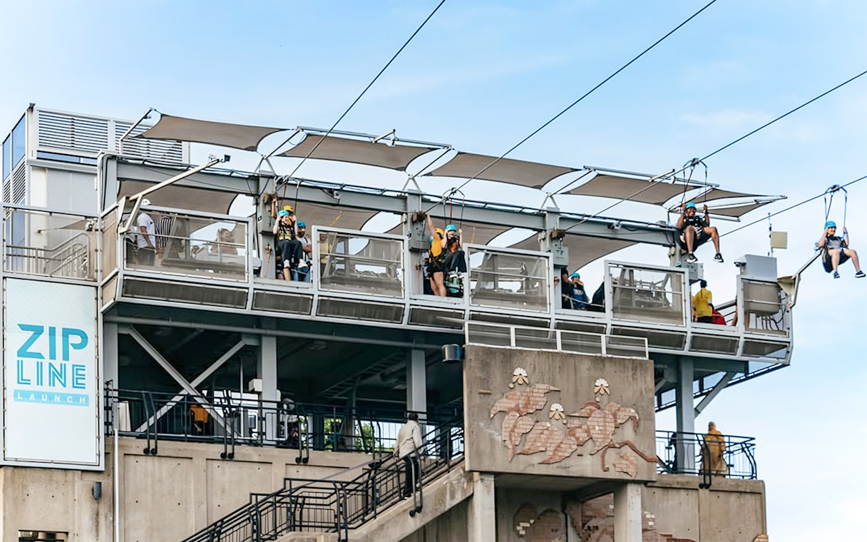 Zipline launch platform with people ziplining towards the falls.