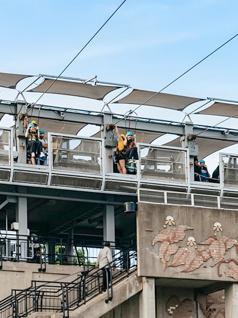 Zipline launch platform with people ziplining towards the falls.