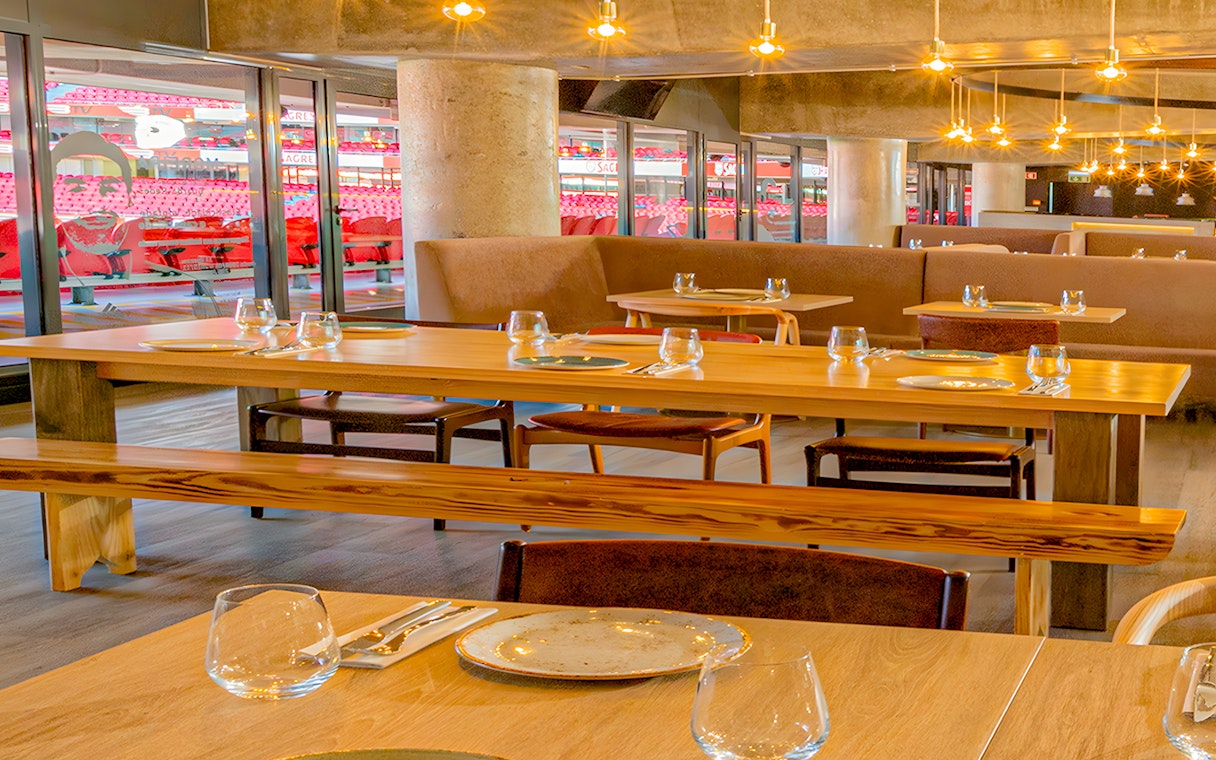 Restaurant interior with tables set, overlooking Benfica Stadium seating area.