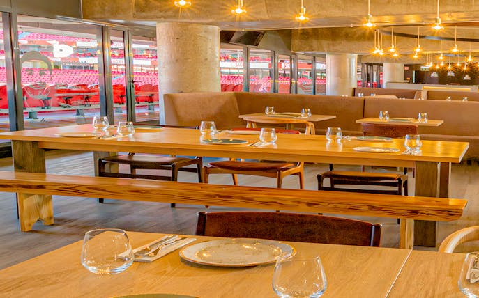 Restaurant interior with tables set, overlooking Benfica Stadium seating area.