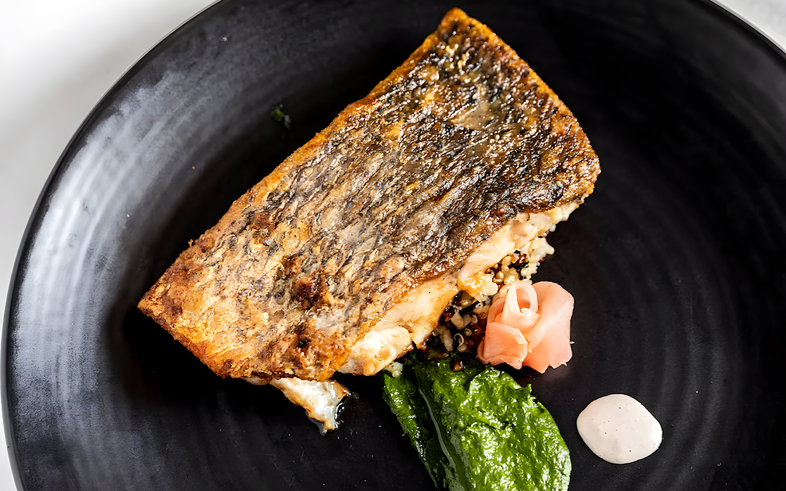 Grilled fish with quinoa, spinach puree, and pickled ginger on a black plate, Starlight Dinner Cruise Sydney.