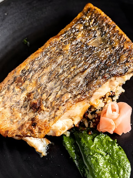 Grilled fish with quinoa, spinach puree, and pickled ginger on a black plate, Starlight Dinner Cruise Sydney.