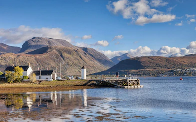 Fort William landscape with Ben Nevis and loch, featuring a small pier and white buildings.
