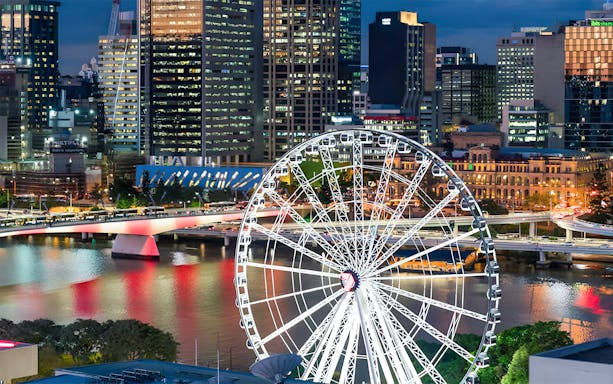 Ferris wheel overlooking Brisbane cityscape at night.