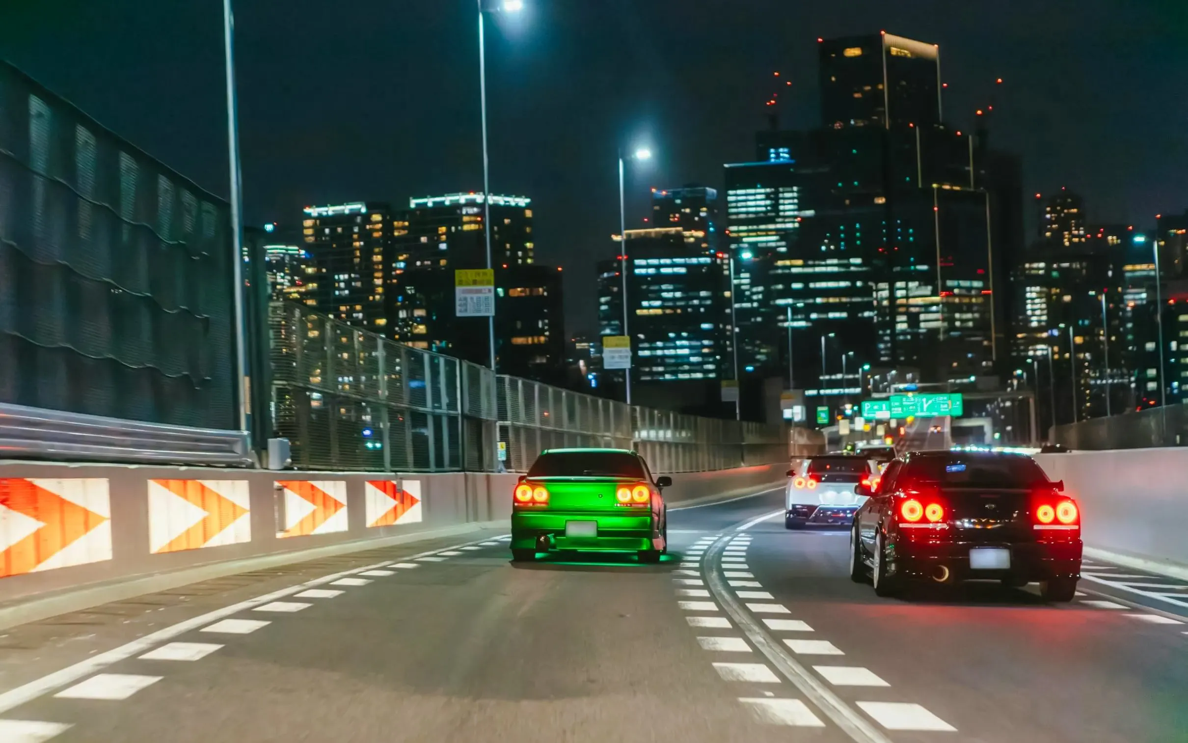 Cars racing on a Tokyo highway at night with city skyline in the background.