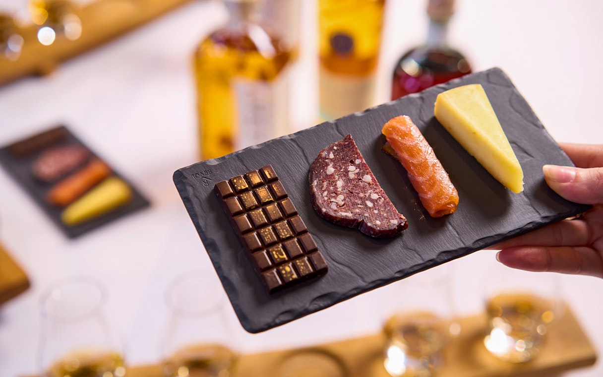 Chocolate, sausage, salmon, and cheese on a slate platter at a tasting experience.