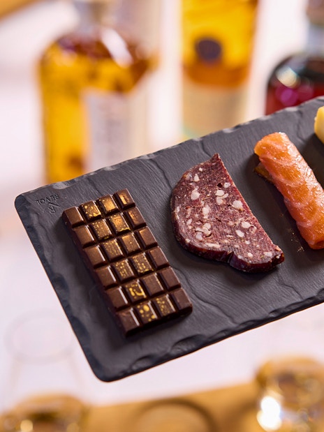 Chocolate, sausage, salmon, and cheese on a slate platter at a tasting experience.
