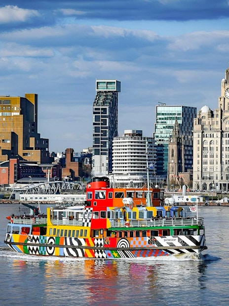 Colorful ferry on River Mersey with Liverpool skyline in the background.