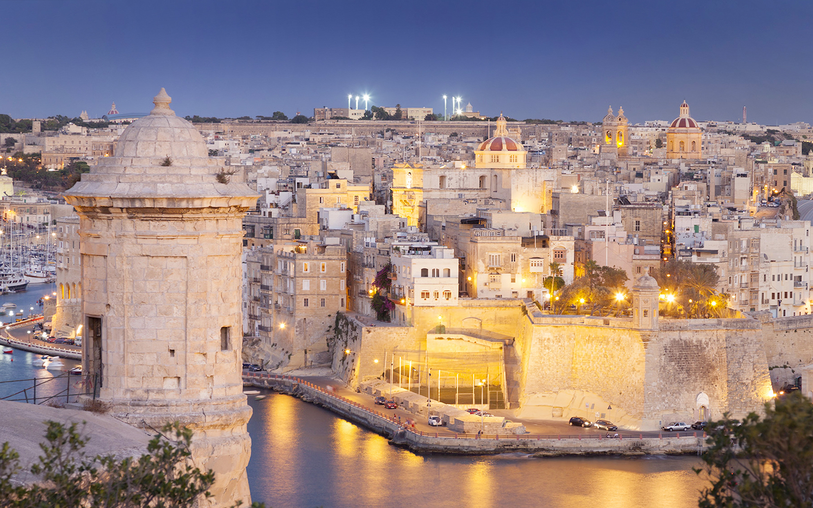 Malta's illuminated cityscape at night with historic buildings and harbor.