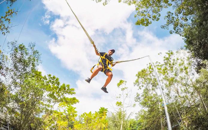 Person swinging on a giant swing at Escape Penang amidst lush greenery.