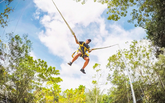 Person swinging on a giant swing at Escape Penang amidst lush greenery.