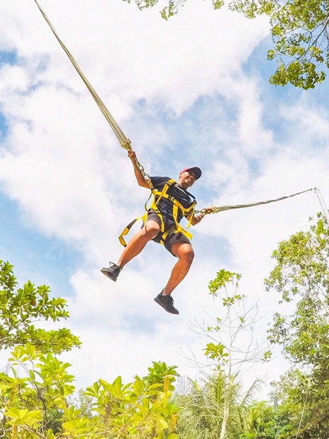 Person swinging on a giant swing at Escape Penang amidst lush greenery.