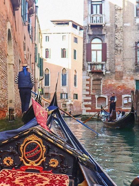 Gondola ride through narrow canal in Venice with tourists and gondolier.