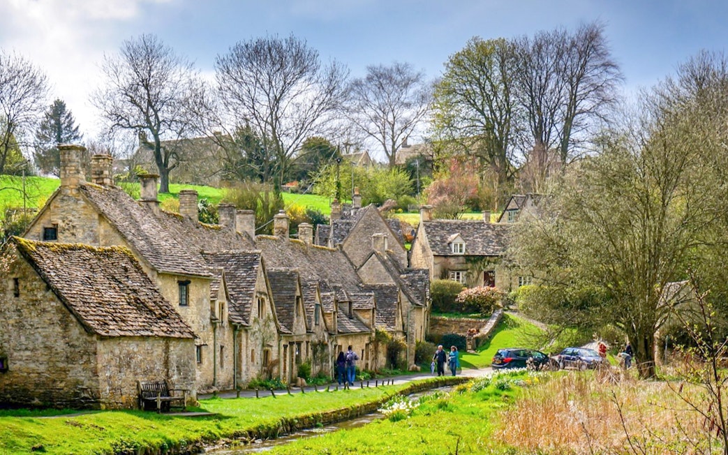 Arlington Row cottages in Bibury Village, Cotswolds, with visitors walking nearby.