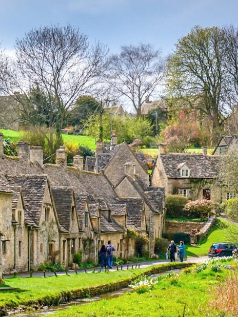 Arlington Row cottages in Bibury Village, Cotswolds, with visitors walking nearby.