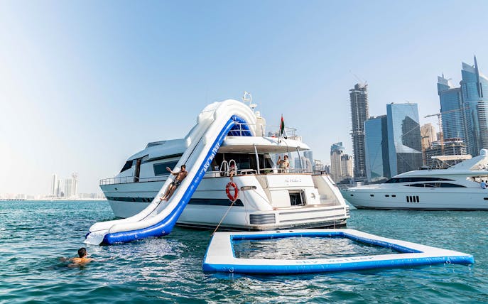Yacht with slide and pool in Dubai Marina with city skyline.