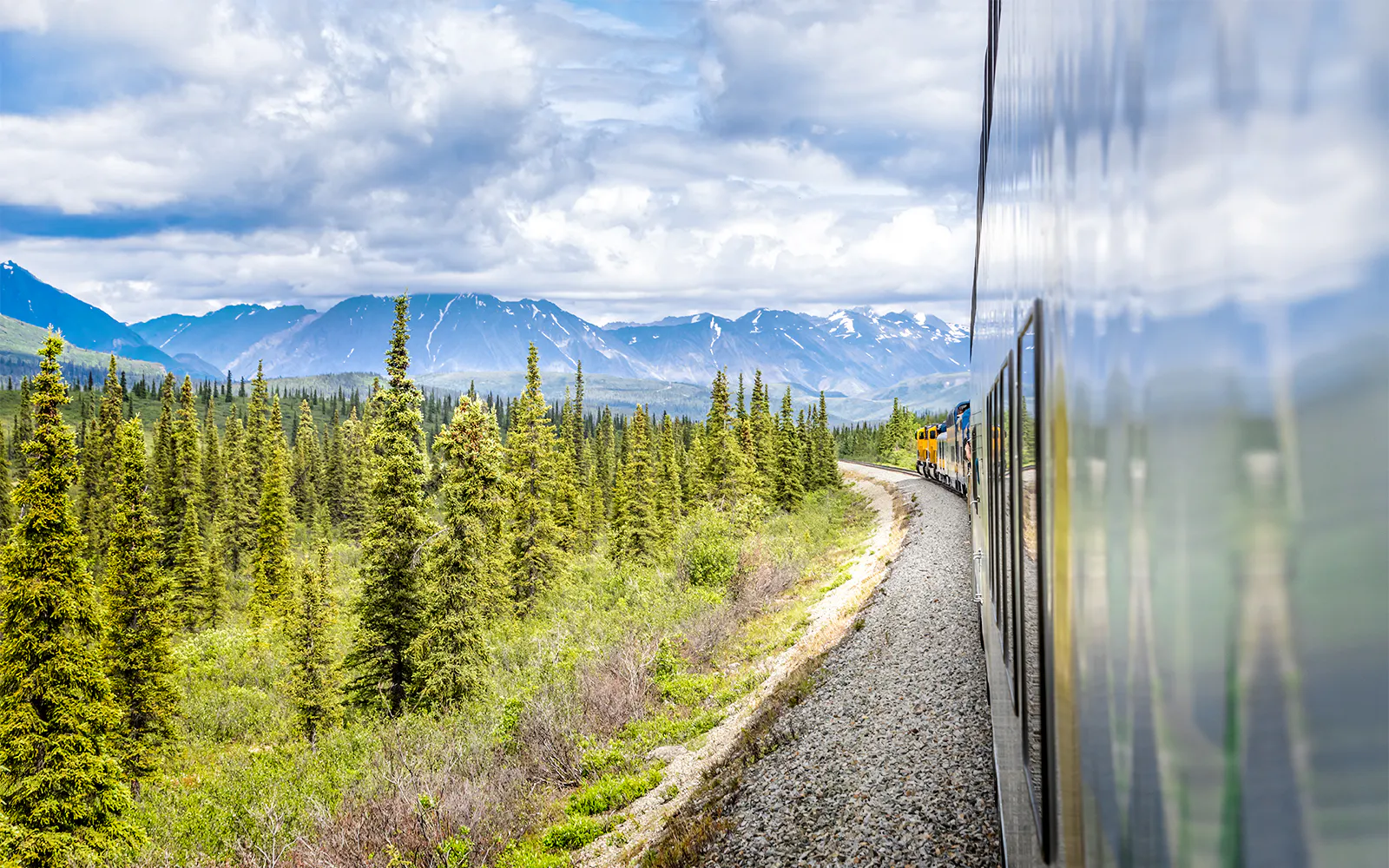 Alaska Railroad train traveling through forested mountains.